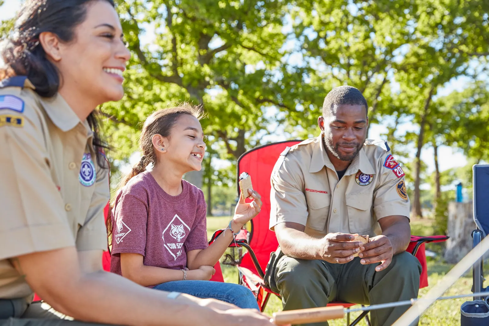 Two Cub Scout leaders in uniform making s'mores with a Scout