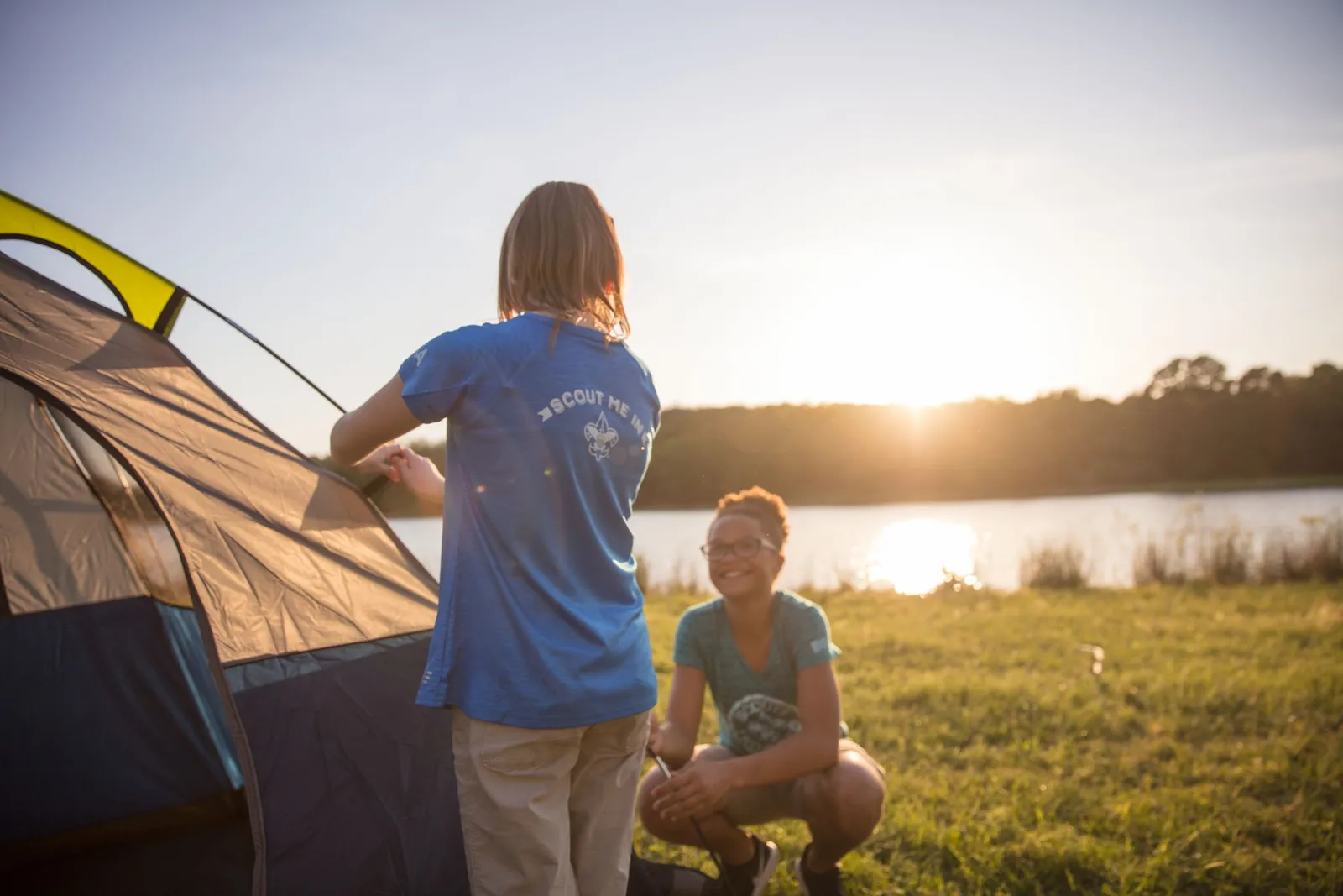 Cub Scouts pitching a tent beside a lake at sunset