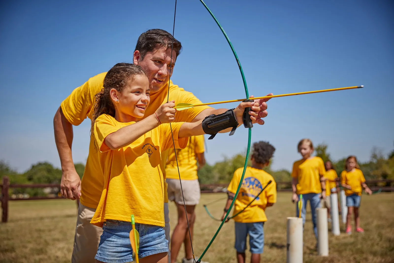 An adult helping a Cub Scout line up a shot at an archery range